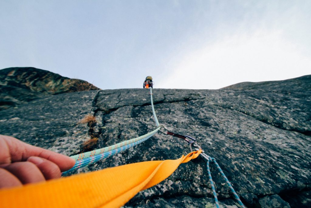 Looking up a rockface with a hand in the foreground grasping mountain climbing rope
